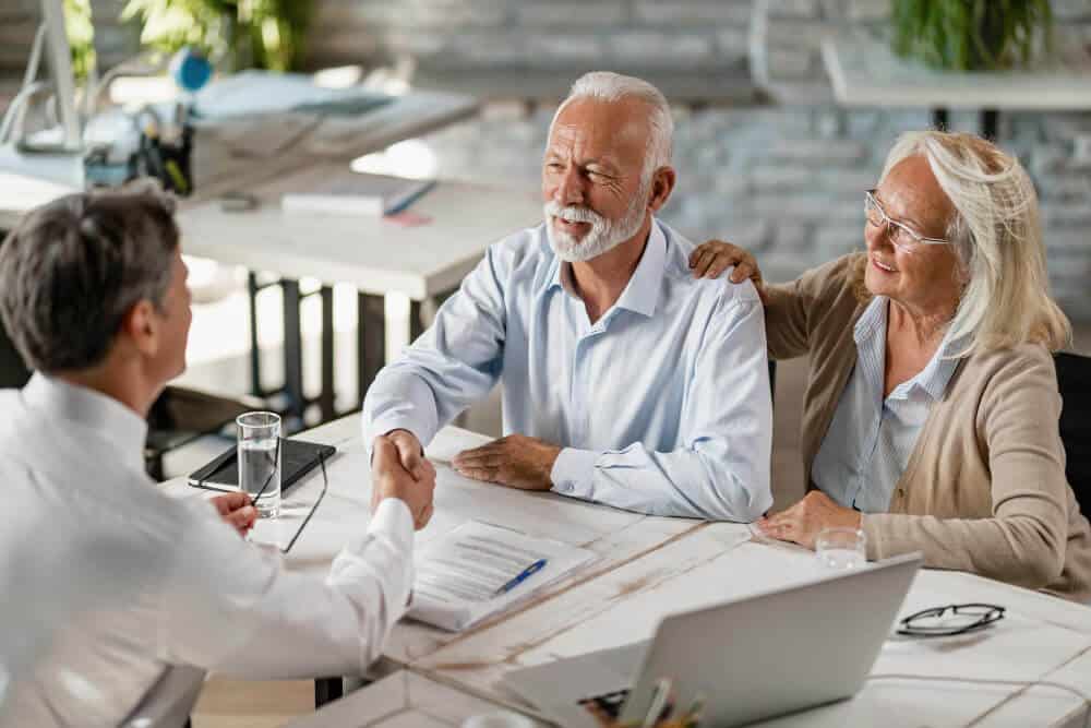 Happy senior couple shaking hands with insurance agent after successful agreement meeting